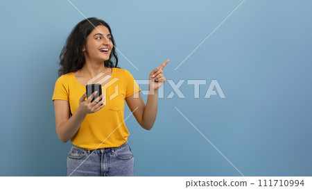 Positive young indian woman with smartphone showing copy space 111710994