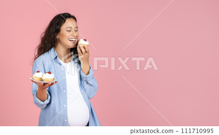 Hungry Expectant Lady Eating Sweets Standing Over Pink Studio Background 111710995