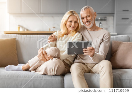 Positive beautiful loving senior spouses using digital tablet at home 111710999