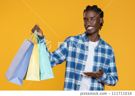 Smiling Young Black Man Demonstrating Bright Shopping Bags In His Hand 111711016