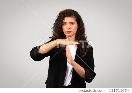 Serious businesswoman in suit making timeout gesture, symbolizing the need for break or pause 111711074