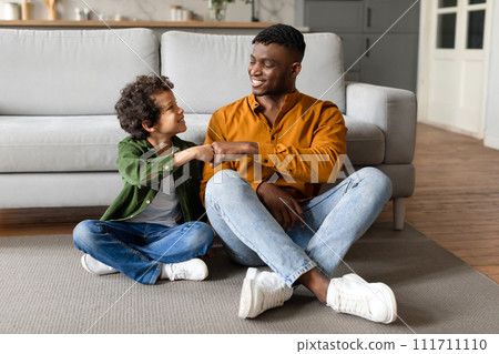 Black boy fist-bumping his father in joyful living room moment 111711110
