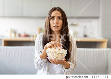 Frightened young woman watching scary movie at home and eating popcorn Frightened young woman watching scary movie at home and eating popcorn 111711111