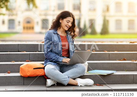 Smiling student indian woman sitting on stairs working on laptop Smiling student indian woman sitting on stairs working on laptop 111711130