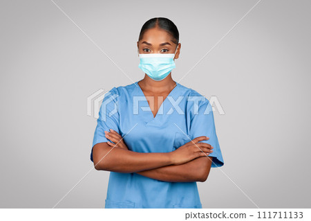 Positive confident black young doctor surgeon, nurse in blue uniform and protective mask with crossed arms 111711133