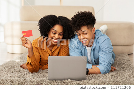 A cheerful young couple is engaged in online shopping, with the woman holding a credit card A cheerful young couple is engaged in online shopping, with the woman holding a credit card 111711206