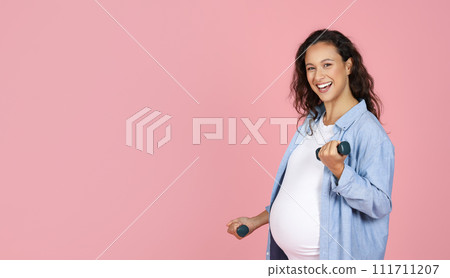 Smiling pregnant brunette lady exercising with barbells on pink background 111711207