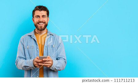 Guy holding smartphone scrolling and texting against blue studio backdrop Guy holding smartphone scrolling and texting against blue studio backdrop 111711213