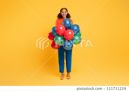 Joyful black teenager girl holds bunch of festive balloons, studio 111711229