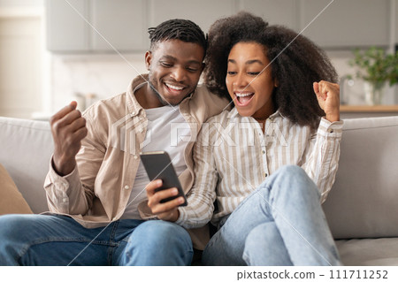 Black Couple Celebrating Success With Cellphone Gesturing Yes At Home 111711252
