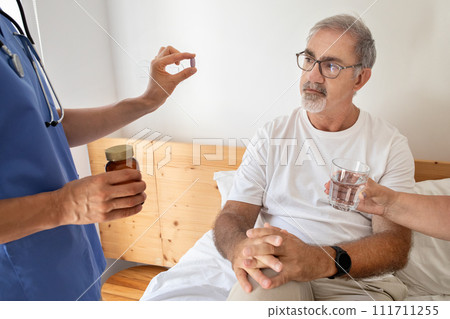Nurse give pill to serious senior caucasian man in bedroom interior 111711255