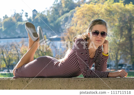 Young woman in a casual dress and sunglasses resting outdoors on a warm autumn day. Young woman in a casual dress and sunglasses resting outdoors on a warm autumn day. 111711518