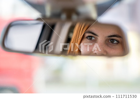 Young woman driver checking rear view mirror looking backwards while driving a car. 111711530