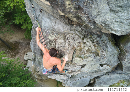 Young man climbing steep wall of rocky mountain. Male climber overcomes challenging route. Engaging in extreme sport concept. 111711552