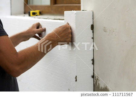 Worker hands installing white rigid polyurethane foam sheet on plastered brick wall. Modern technology, renovation, insulation concept. Worker hands installing white rigid polyurethane foam sheet on plastered brick wall. Modern technology, renovation, insulation concept. 111711567
