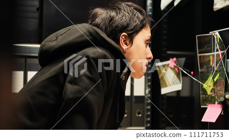 Law officer reviewing clues and proof in agency evidence room, conducting criminal police investigation. Investigator evaluating classified documents and surveillance material. Handheld shot. 111711753