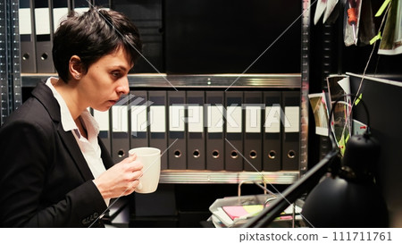 Private detective conducts investigation in police archive incident room, examining forensic results evidence and classified records. Investigator looking for incriminating proof. Handheld shot. 111711761