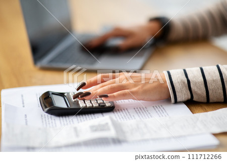Focused woman calculating finances with a calculator and laptop at a wooden desk 111712266