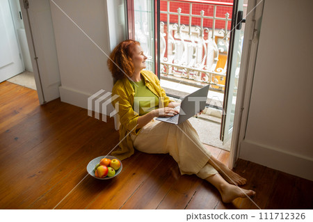 Senior Woman Relaxing With Laptop On Floor Near Open Window At Home Senior Woman Relaxing With Laptop On Floor Near Open Window At Home 111712326