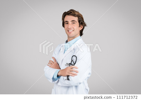 Smiling confident male therapist in white coat holding stethoscope, crossed arms on chest isolated on gray background 111712372