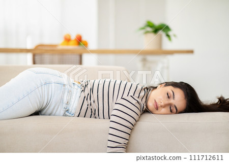 Tired young pretty arab woman sleep with closed eyes on sofa in light living room Tired young pretty arab woman sleep with closed eyes on sofa in light living room 111712611