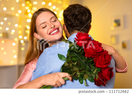 Joyful woman embracing man, holding red roses with festive lights 111712662