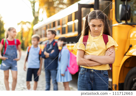 Unhappy young girl standing by herself next to yellow school bus Unhappy young girl standing by herself next to yellow school bus 111712663