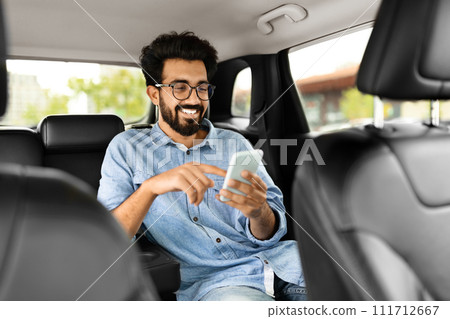 Cheerful indian guy chatting with friends while sitting in taxi 111712667