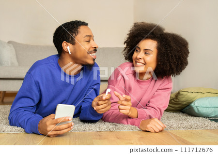 African couple relaxes listening music on phone using earbuds indoor 111712676