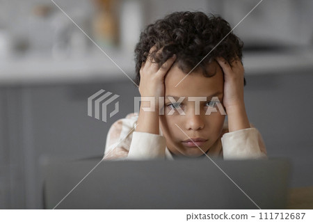Little black boy feeling stressed and worried while looking at laptop screen, 111712687