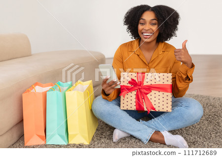 Happy African American woman with a wide smile holding a gift and her smartphone Happy African American woman with a wide smile holding a gift and her smartphone 111712689