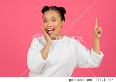 Excited asian woman with hair buns pointing upwards with finger 111712757