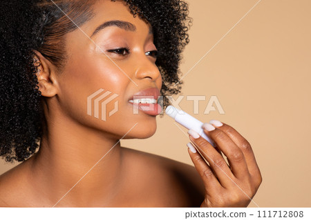 Black woman applying lip balm, profile view, beige background Black woman applying lip balm, profile view, beige background 111712808