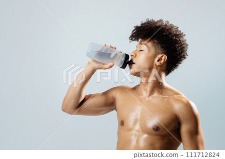 Fit man hydrating after workout posing with water bottle, studio Fit man hydrating after workout posing with water bottle, studio 111712824