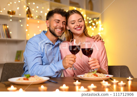 Cuddling couple toasting wine glasses in a romantic setting 111712906