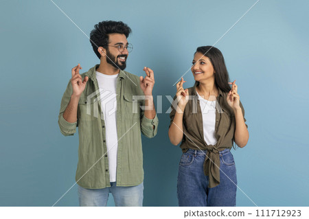 Happy indian man and woman crossing fingers, blue background 111712923