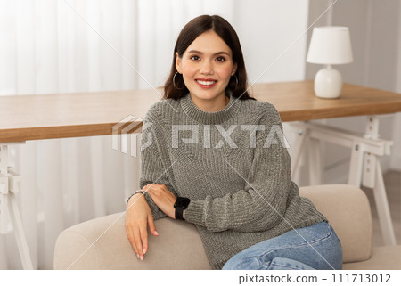 Pretty young woman sitting on couch at home Pretty young woman sitting on couch at home 111713012