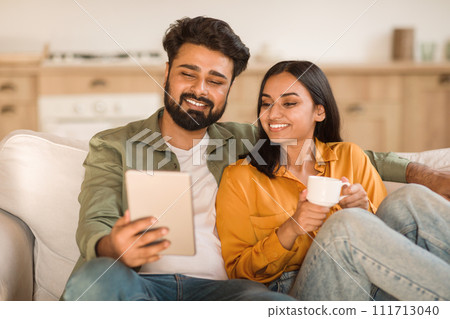 Hindu couple with tablet and coffee on sofa 111713040