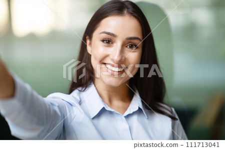 Glad arab young businesswoman with friendly smile take selfie, in modern office building Glad arab young businesswoman with friendly smile take selfie, in modern office building 111713041