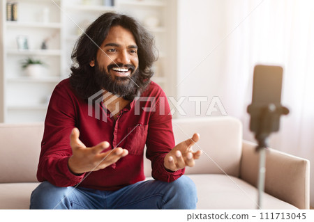 Indian guy vlogger streaming from home, using phone on tripod 111713045