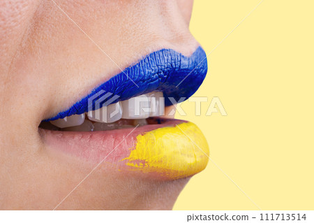 Close up of beautiful and plump female lips painted in blue and yellow. Lips of woman painted in Ukrainian flag colors. Close up of beautiful and plump female lips painted in blue and yellow. Lips of woman painted in Ukrainian flag colors. 111713514