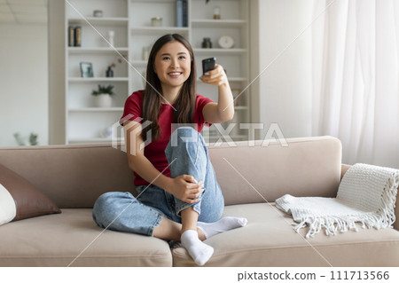 Happy asian woman with remote controller in hand watching tv at home 111713566