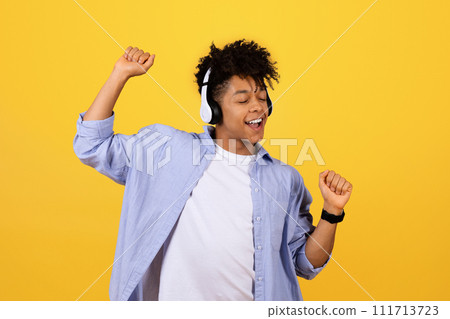 Happy black guy dancing with headphones on yellow background 111713723