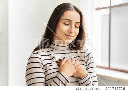 Cheerful calm young arab lady with closed eyes press hands to chest heart, make thanks sign 111713726