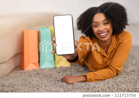 Glad millennial african american curly lady with bags show smartphone with empty screen 111713750