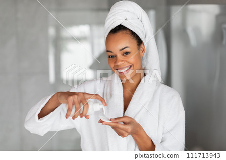 black woman dispenses lotion into cotton pad in modern bathroom 111713943