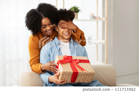 A joyful woman playfully covers a man's eyes from behind, both smiling with anticipation A joyful woman playfully covers a man's eyes from behind, both smiling with anticipation 111713982
