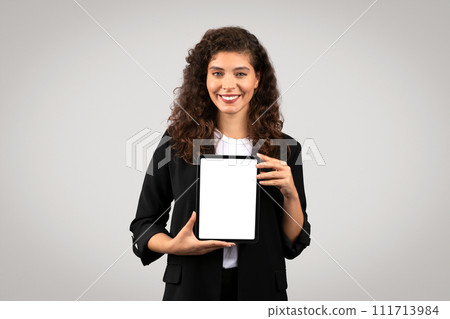 Cheerful young businesswoman presenting digital tablet with white blank screen, demonstrating business apps or website 111713984