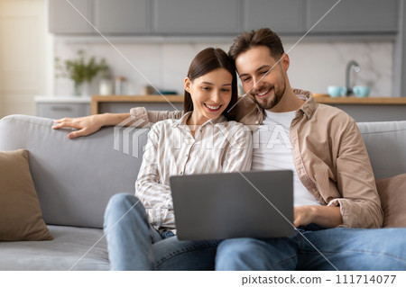 Couple smiling and using laptop computer on couch at home 111714077