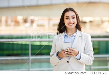 Glad pretty confident young caucasian woman in suit enjoy work, typing on smartphone outdoors 111714172